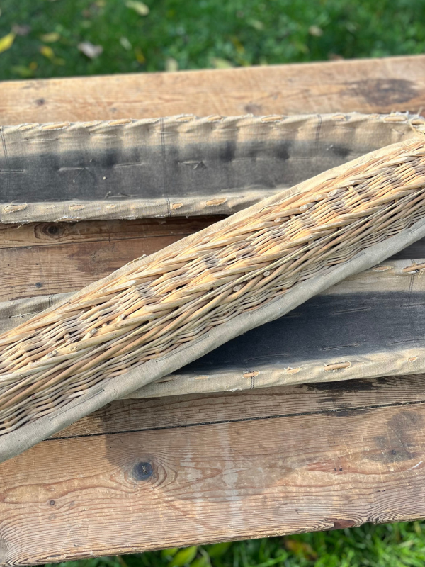 Underside detail of three long vintage French baguette baskets lined in natural linen. Placed on a pine garden table.