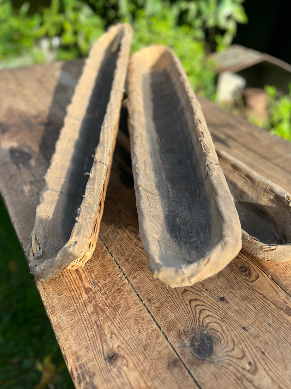 Three long vintage French baguette baskets lined in natural linen. Placed on a pine garden table.