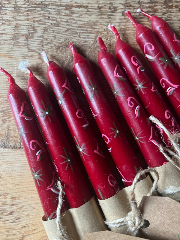 Close up of red hand painted folklore candles wrapped in brown paper & string laying flat on a wooden table