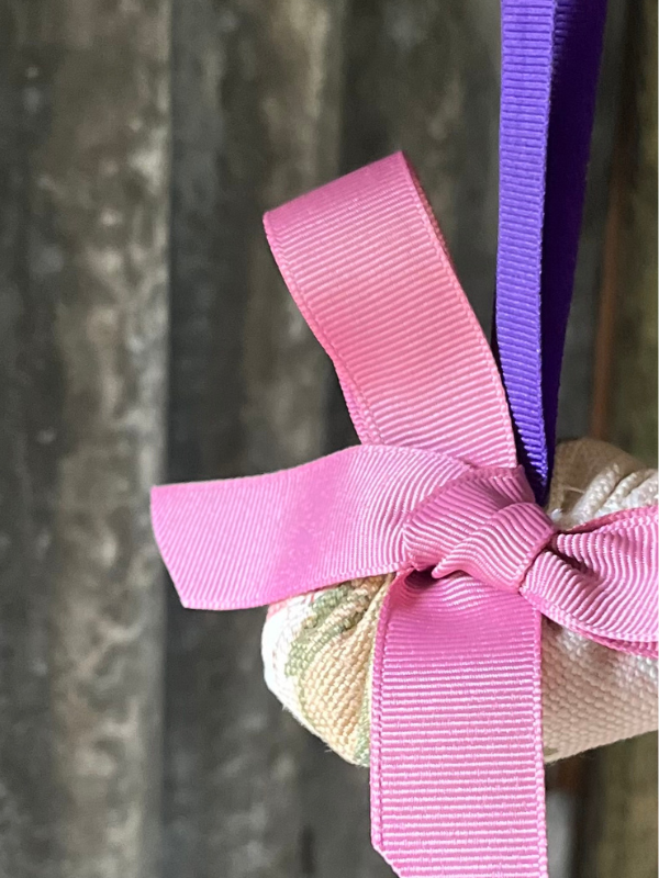 Close up of a small vintage fabric Christmas decoration hanging from a twisted tree branch. With a bright pink grosgrain ribbon bows on the front. Against a rusty corrugated iron background.