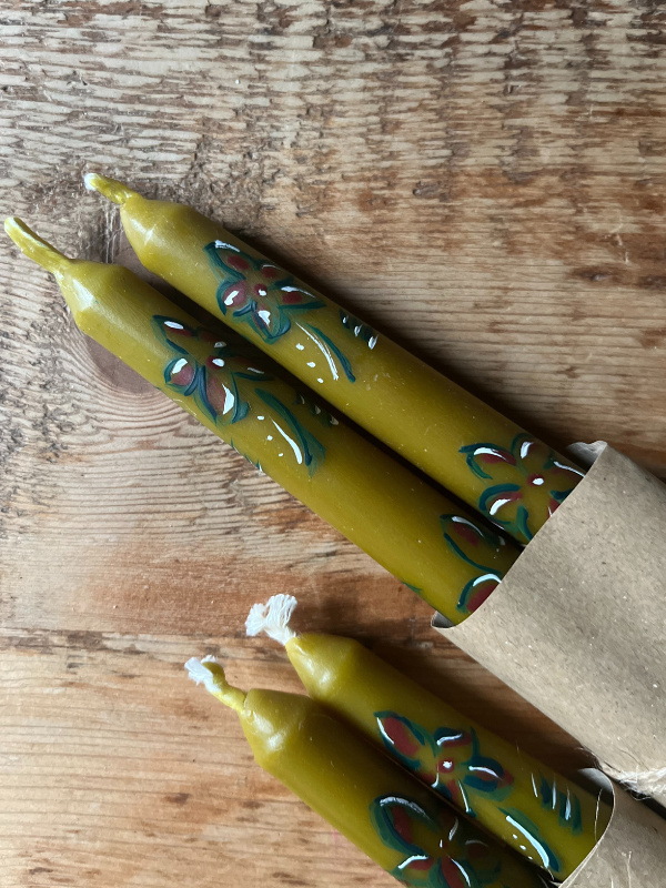 Close up of sage green hand painted floral candles wrapped in brown paper & string laying on wooden table