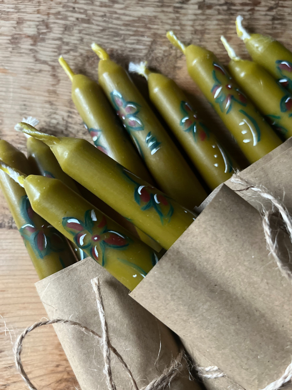Close up of group of green hand painted candles wrapped in brown paper & string laying on wooden table