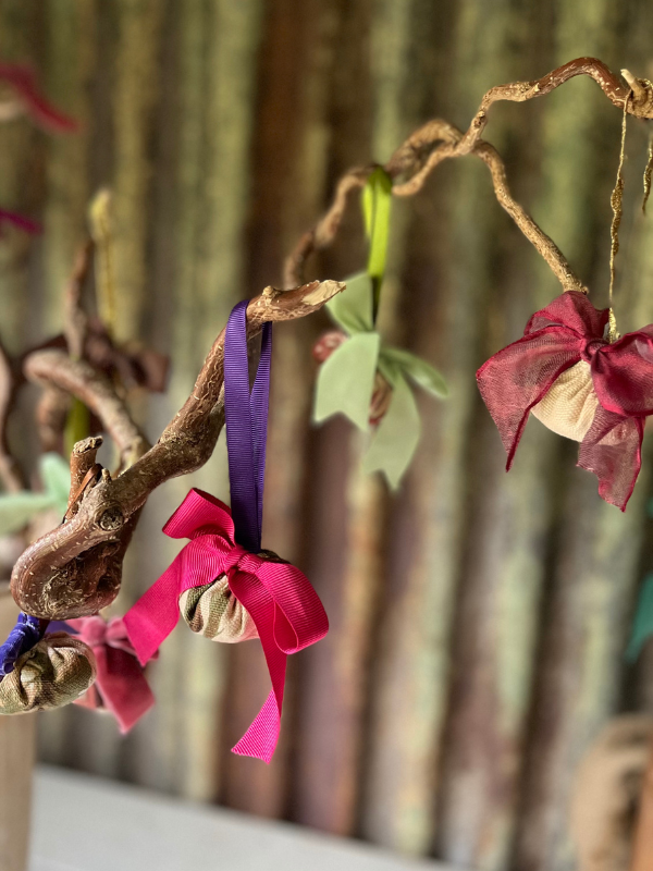 Close up of a small assortment of vintage fabric decoration hanging from a twisted tree branch. Multi-coloured bright ribbon bows on the front. Against a rusty corrugated iron background.