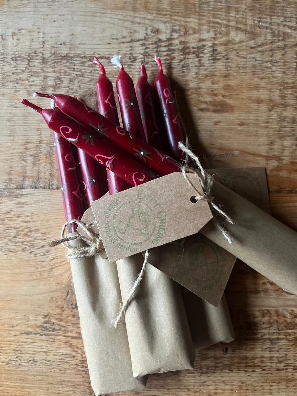 Group of red hand painted candles wrapped in brown paper & string laying on wooden table