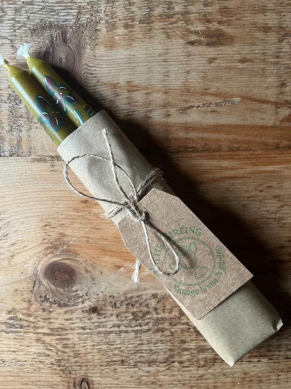 Pair of green hand painted candles wrapped in brown paper & string laying on wooden table
