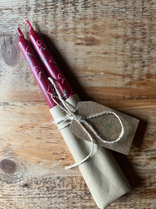 Pair of red hand painted folklore candles wrapped in brown paper & string laying flat on a wooden table