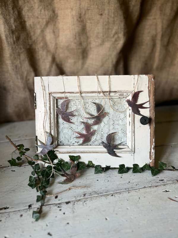 Small white wooden window frame with lace curtain strung with brown tiny swallow bird bunting