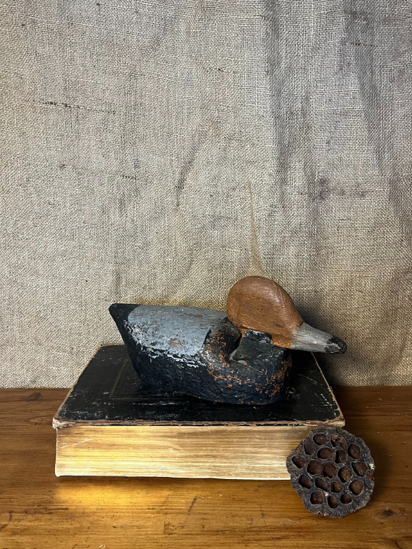 Antique wooden decoy duck sitting on an old book facing right