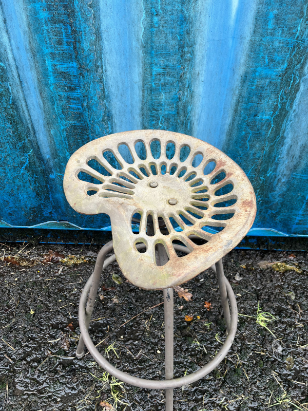 Close up of top view of a grey industrial tractor seat stool against a blue shipping container