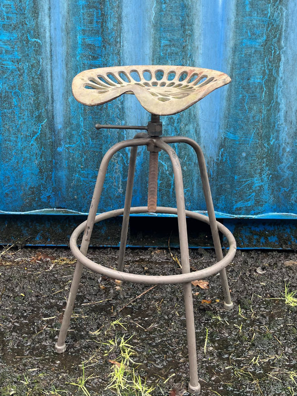 Close view of grey industrial tractor seat stool against a blue shipping container