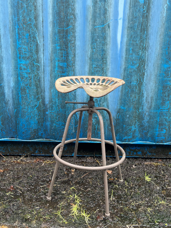 Grey industrial tractor seat stool against a blue shipping container