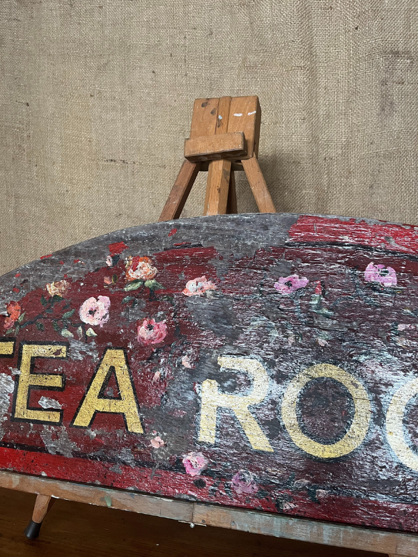 Right hand view of antique Tea Room sign gold letters on red painted background with pink roses