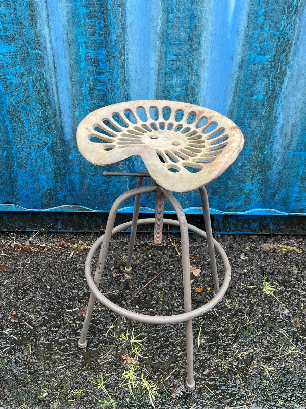 Top view of a grey industrial tractor seat stool against a blue shipping container
