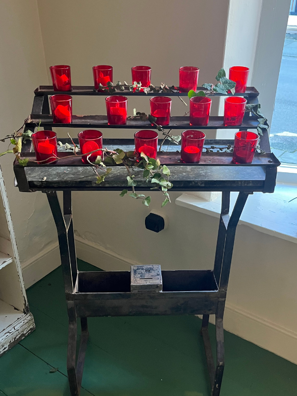 Antique church votive stand with red glass candle holders draped in ivy