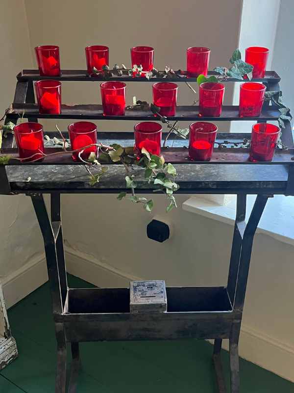 Close shot of an antique church votive stand with small red glass candle holders draped in ivy