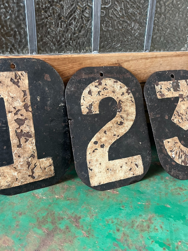 Close up of vintage black & white metal numbers 123 propped up against a wooden cupboard