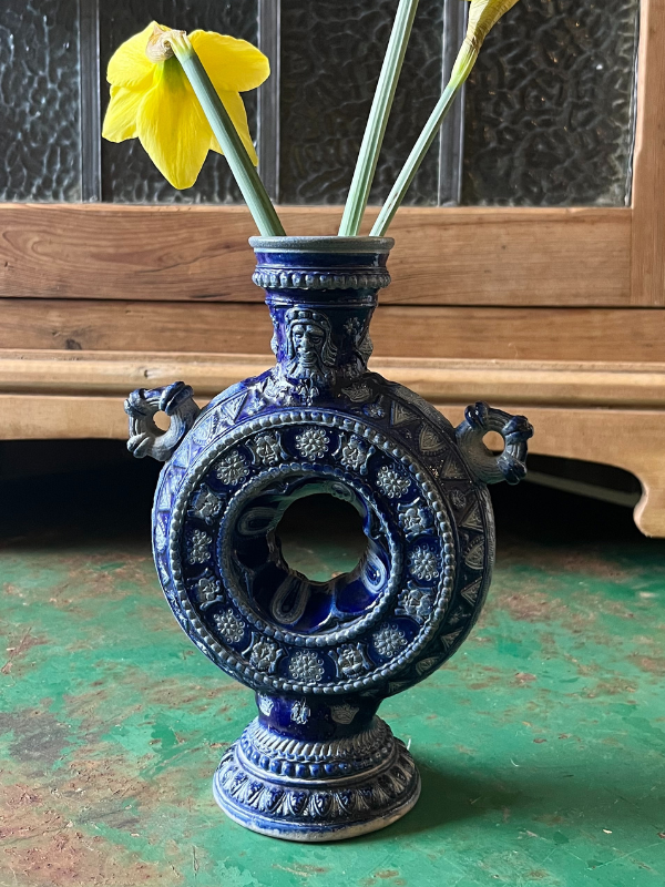 Close view of a blue 7 white tulipiere vase with daffodils on a green metal table