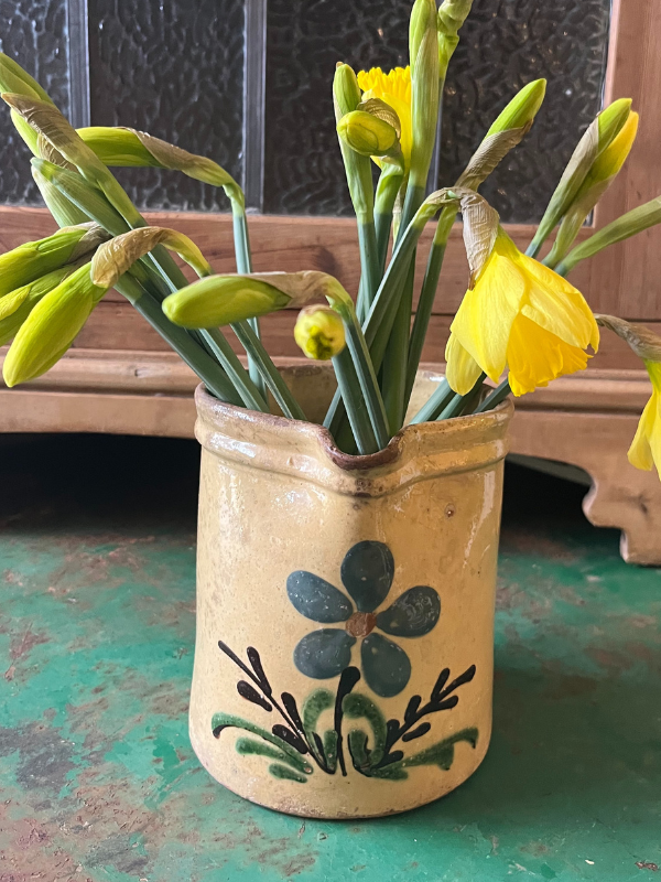 Close view of a glazed jug with daffodils on a green metal table