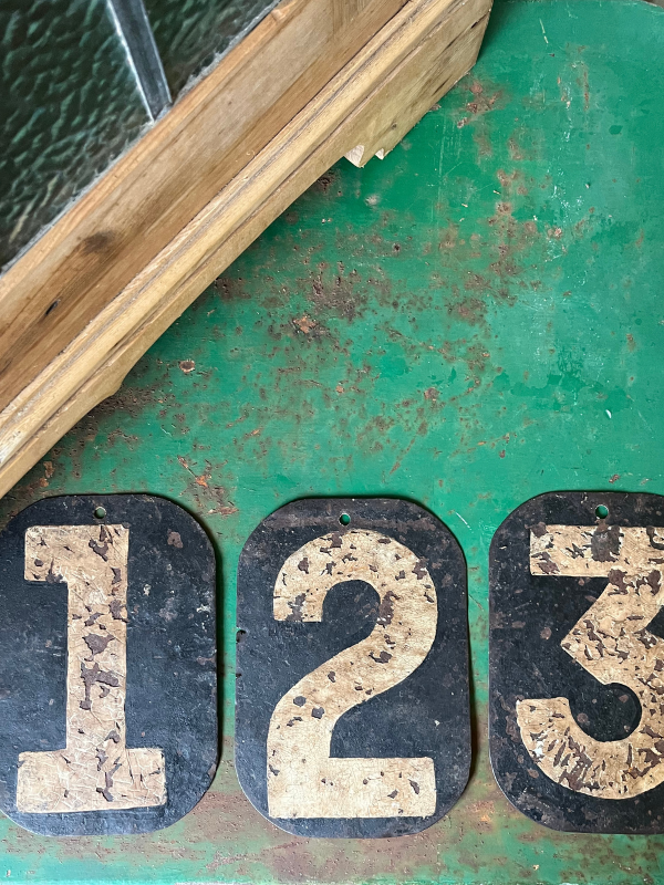 Flat lay of 3 black & white metal numbers on a distressed green table