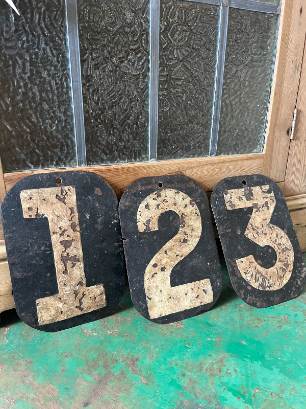 Black & white vintage metal numbers 123 propped up against a wooden cupboard