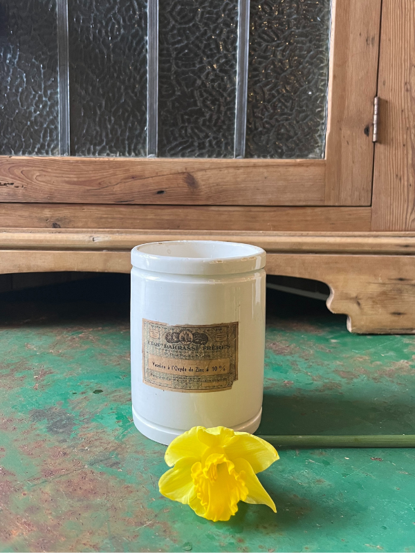 White French Vaseline pot with a single daffodil laying on a green table