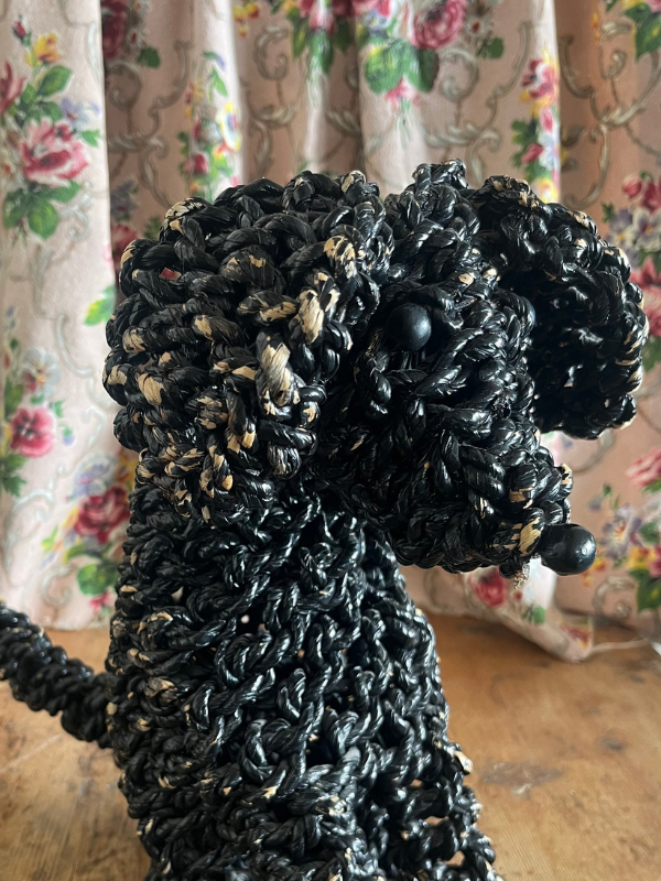Close up shot of a black rope poodle dog on a wooden table with a floral fabric background