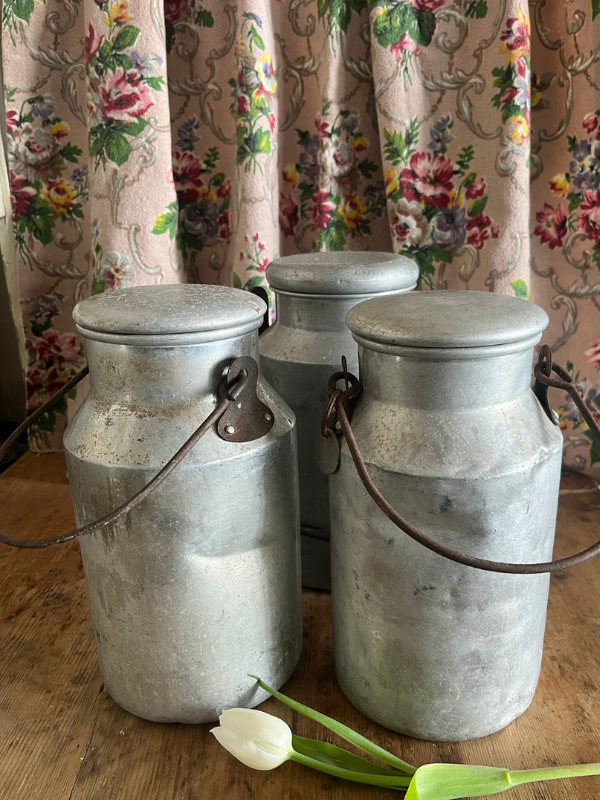 Group of three metal milk churns against a floral fabric background
