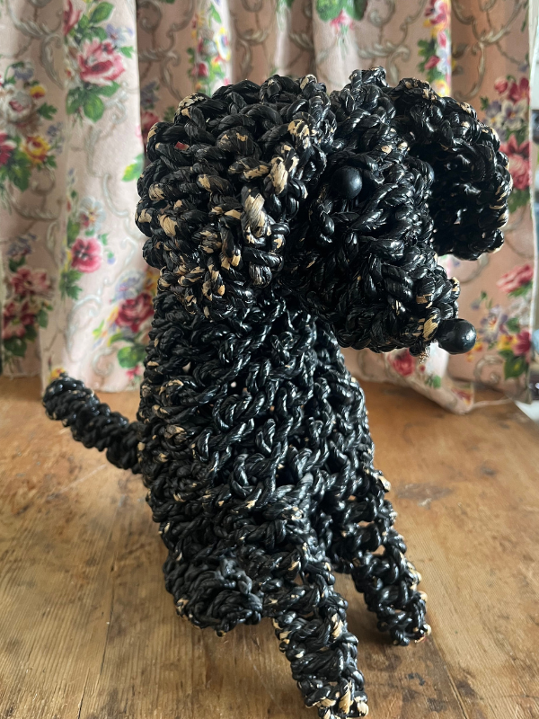 Right hand side of a black rope poodle dog on a wooden table with a floral fabric background