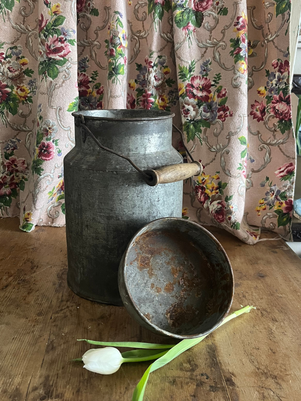 Dark metal milk churn against a floral fabric background