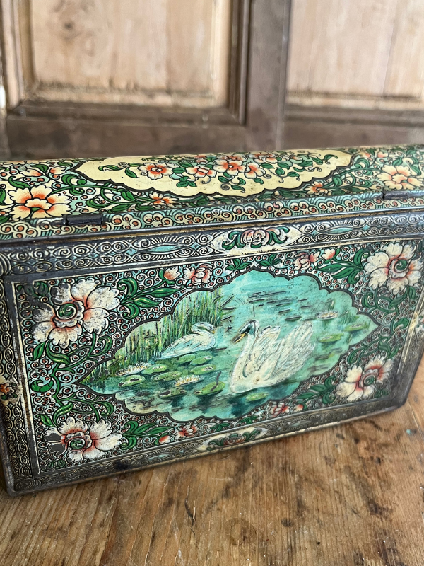 Front view of a highly decorated vintage tin on a wooden table showing swan image