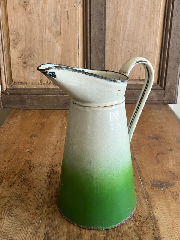 Left facing view of a two tone green & white enamel jug on a wooden table