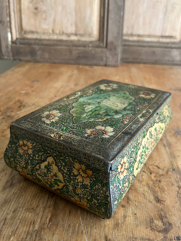 Side view of a highly decorated vintage tin on a wooden table showing floral side panels