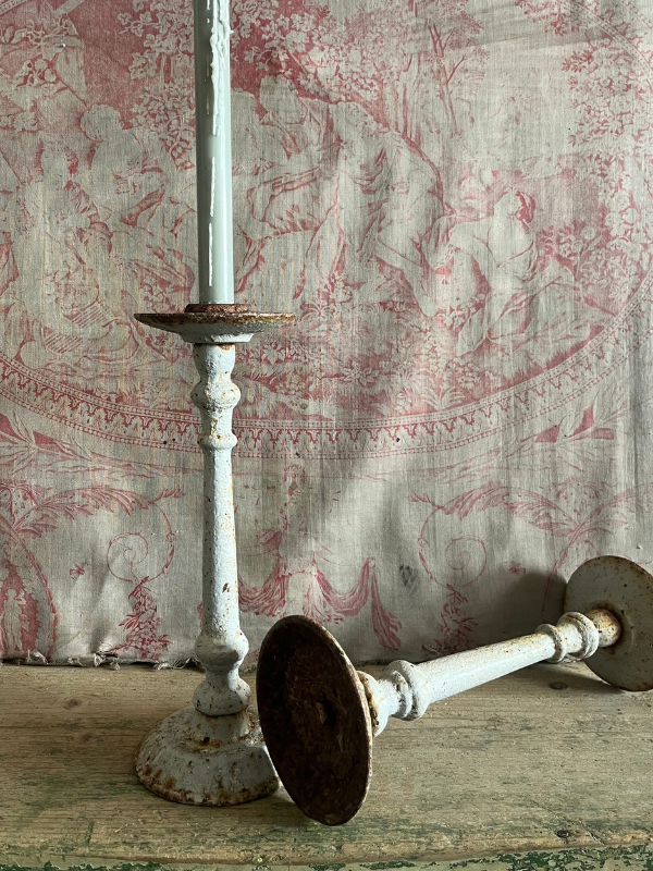 Close up of a pair of worn rusted grey cast iron candlesticks against pink toile de jouy fabric