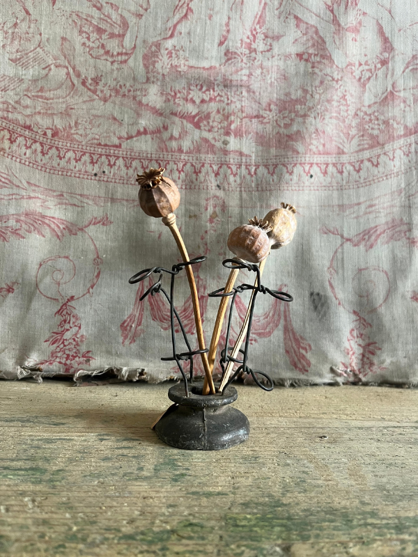 Dried poppy seed heads sitting in a metal FloralAid flower holder against pink toile de jouy fabric