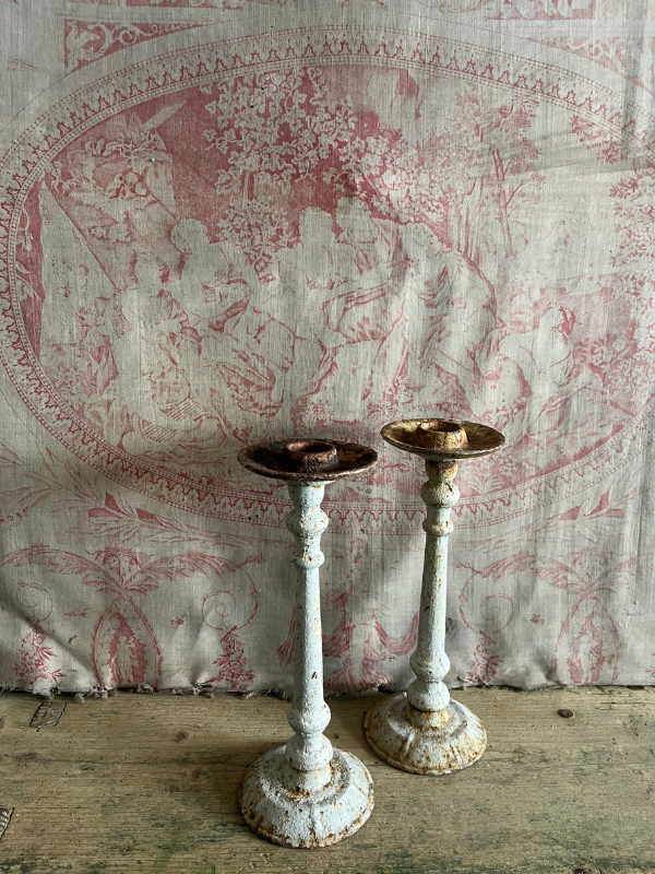 Pair of worn rusted grey cast iron candlesticks against pink toile de jouy fabric.