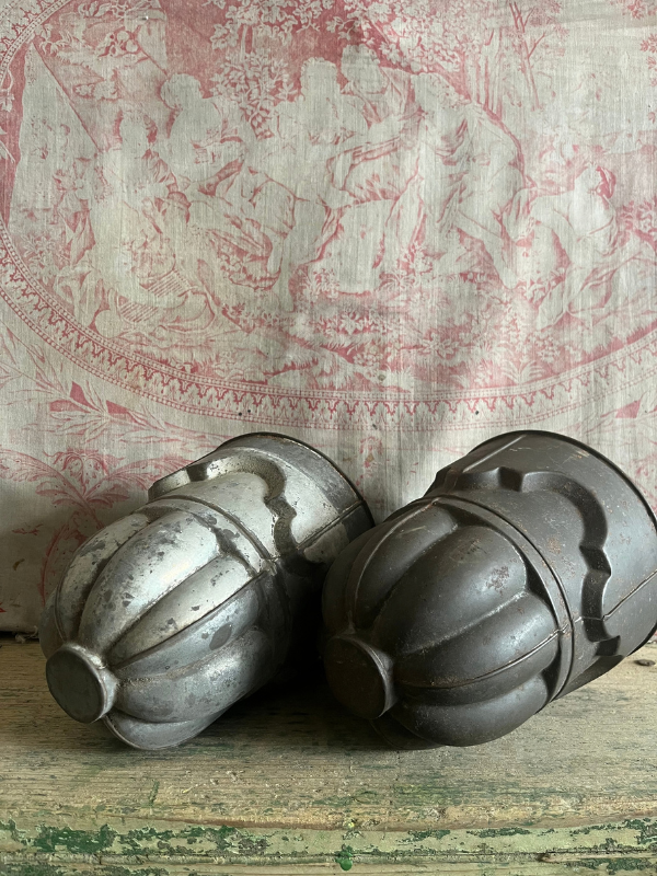 Pair of vintage detailed metal jelly moulds laying side by side on a green wooden bench