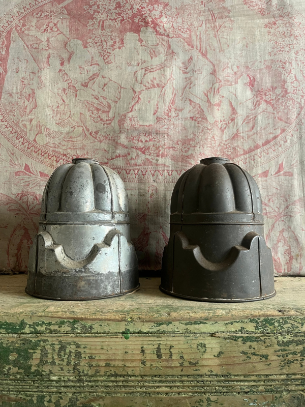 Pair of vintage detailed metal jelly moulds standing side by side on a green wooden bench