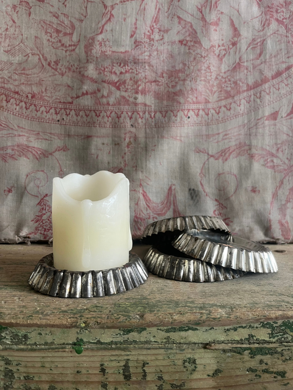 Pile of vintage patisserie tins with a candle in the background against pink toile de jouy fabric