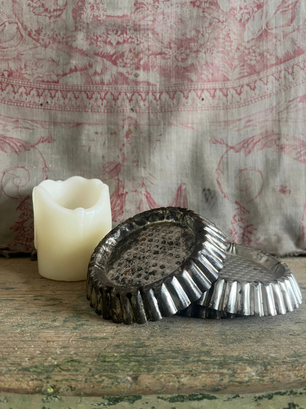 Pile of vintage patisserie tins with a candle in the background against pink toile de jouy fabric
