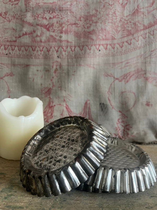 close view of a pile of vintage patisserie tins with a candle against pink toile de jouy fabric